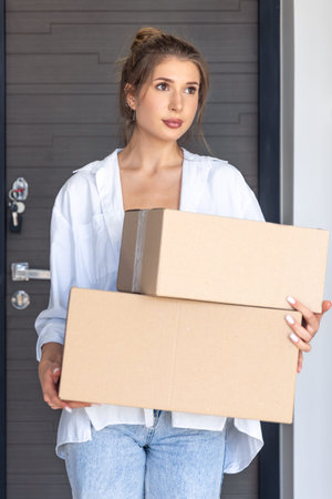 Young woman holds boxes by a closed door after delivery. Online shopping.