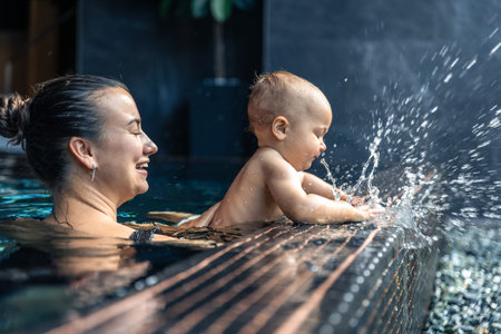 Baby splashes at pool edge, laughter and spray. Playful game in spa.