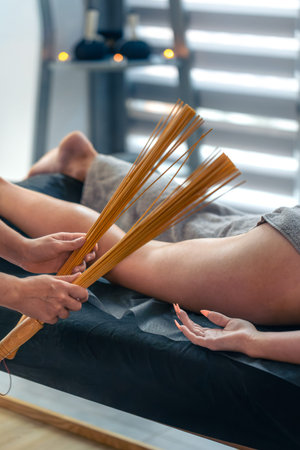 Bamboo whisk on thigh in bright spa. Percussive drainage.の写真素材