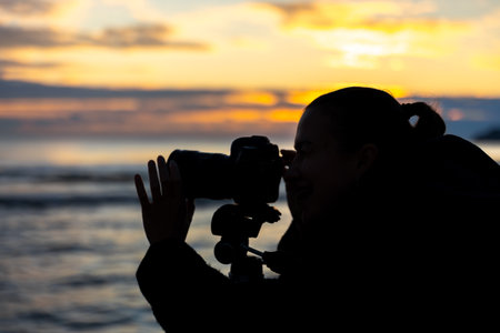 Photographer with camera by the sea at sunset. Girl silhouette with camera.の写真素材