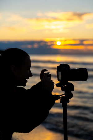 Silhouette of smiling girl with camera at sunset. Youthful vibe.の写真素材