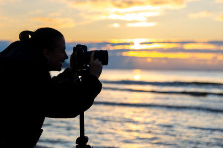 Girl photographing sunset by the sea. Silhouette of woman with camera.の写真素材