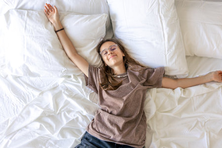 Teen softly stretching on pillows with a morning smile. Quiet morning home.の写真素材