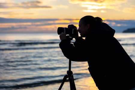 Woman photographer near waves at sunset. Girl shooting the sea.の写真素材