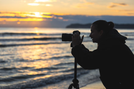 Woman photographing ocean sunrise. Silhouette with camera.の写真素材