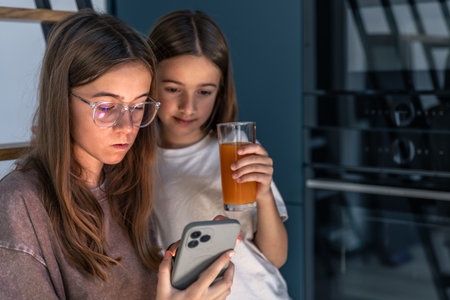 Two girls in the kitchen, focused look at smartphone and glass of juice. Moment of focus.の写真素材