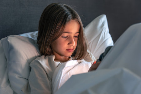 Girl gazing at smartphone under duvet. Evening scroll.の写真素材