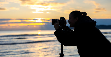 Photographer at the sea in evening light. Girl with camera at sunset.の写真素材