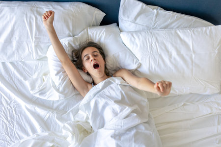 Girl waking with a yawn arms wide. First stretch.