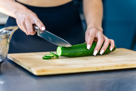 Woman slices cucumber in kitchen closeup. Fresh salad.の写真素材