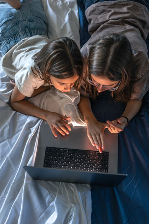 Two girls in bed with laptop, joyful focus. Smiling girl.の写真素材