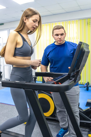 Doctor monitors treadmill for woman in rehabilitation gym. Gait recovery.
