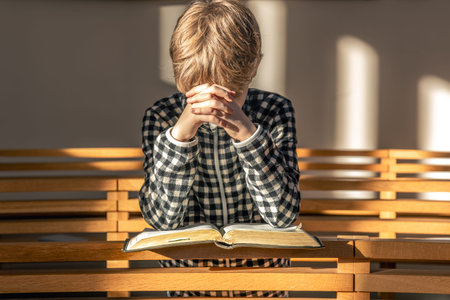 A child in prayer with a Bible inside a bright church. Prayer and light.