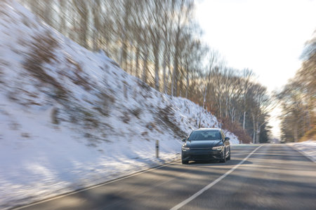 Black modern sedan driving on snowy forest road in winter. Dynamic travel scene.の写真素材