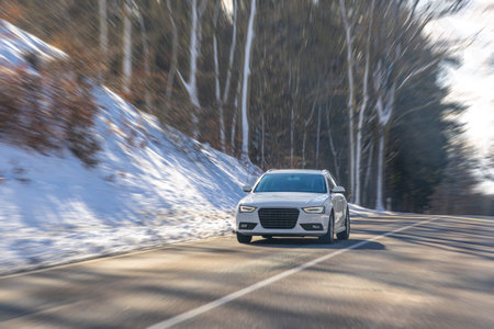 White sedan driving on snowy forest highway in winter. Modern car on road.の写真素材