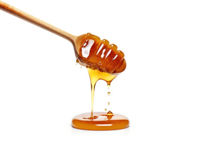 Honey dripping from a wooden honey dipper isolated on white backgroundの素材