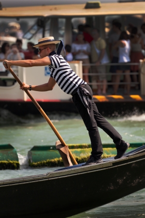 Traditional dress for a Venice gondolier is a beribboned straw hat, striped vest and black trousers. The gondolier stands upright and pushes on the oar torow the boat in the direction he is facing.のeditorial素材