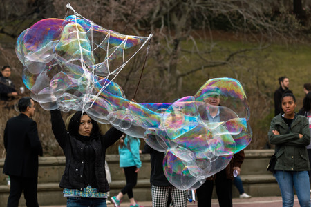 NEW YORK - MARCH 12 2016: Street performer blowing soap bubbles in Central Park. A soap bubble is a very thin film of soapy water enclosing air that forms a hollow sphere with an iridescent surface.のeditorial素材