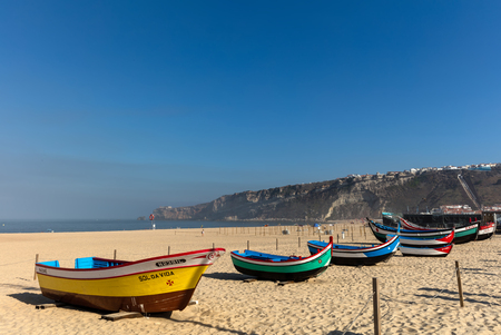 Praia da Nazare beach in Nazare,  Portugal.  Historic examples of the colorful fishing boats used by the local fishermen not so long ago.のeditorial素材
