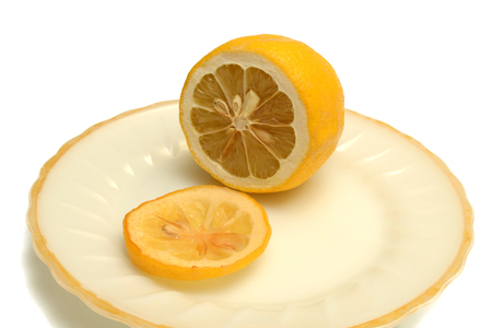 Lemon and a wrung lemon slice on a plate on a white backgroundの写真素材
