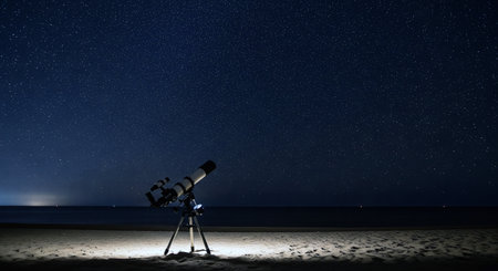 Telescope on a tripod on a beach looking at a starry night sky with a full view of the galaxyの素材