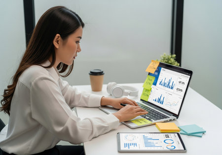 Focused Female Professional Working on Laptop and Tablet with Data Analysisの素材