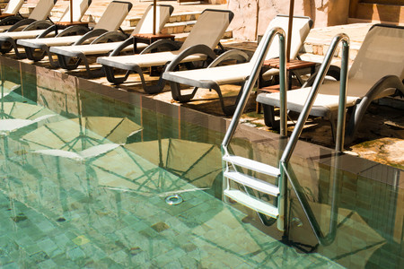 Swimming pool with stair at hotel sounding by beach lounge chairs and umbrellaの写真素材