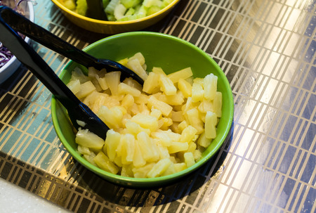 Green bowl contains of pineapple pieces in salad bar with black tong.の写真素材