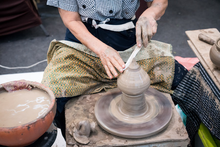 Senior potter's hands shaping decorative clay hollow sculpture on pottery wheel with knife. Cultural handmade showcase in art craft exhibition.の写真素材