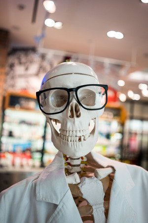 Skull head wearing eyeglasses and white scientific lab coat. Educational material for display against blurred background.の写真素材