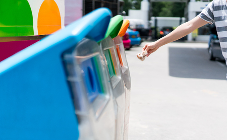 Woman hand putting used paper in recycled bin at parking area. Different color trash cans in row for waste management. Perspective disposal view for saving environmental concept.の写真素材