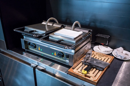 Electric double-stove operated waffle maker for breakfast serving on stainless counter at luxury hotel. Durable square waffle machine for commercial use.の写真素材
