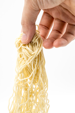Closed up hand pulling uncooked egg noodle isolated on white background.の写真素材