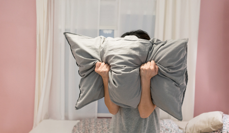 Depressed woman covering her face with pillow and screaming in anger in her roomの写真素材