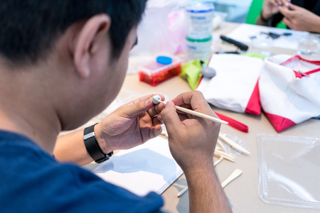 Asian man is trying to model a character design using white clay and wood stick