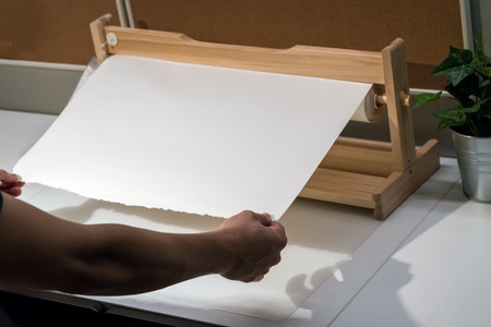 Lady hands pulling white drawing paper roll from wood holderの写真素材