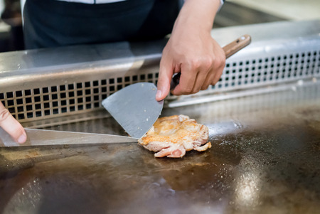 Hand of Chef cooking chicken steak on hot pan in front of customers. Japanese Tepanyaki Steakの写真素材