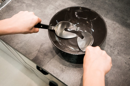 Woman hands holding cooking spoon and fork over black porcelain bowl on kitchen table.の写真素材