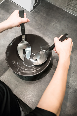 Woman hands holding cooking spoon and fork over black porcelain bowl on kitchen table.の写真素材