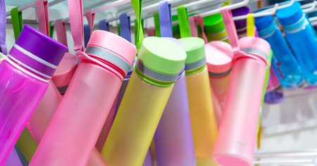 Rows of colorful drink bottles with fabric hand strap handing on metal rack.の写真素材