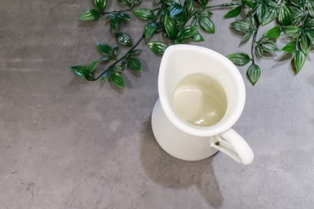White metal pitcher on grey background with green leaves.の写真素材