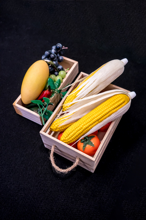 Artificial colorful fruits in wooden boxes on black carpet for backgroundの写真素材