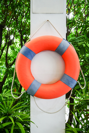 Orange Lifesaving Float hanging on white concrete with nature backgroundの写真素材