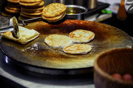frying round roti dough in hot pan with vegetable oil by street.