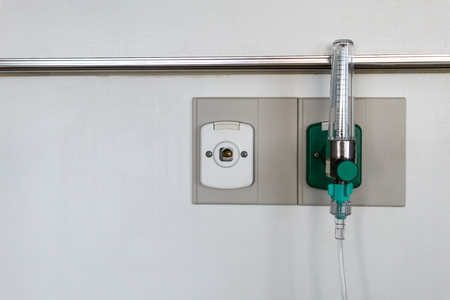 Oxygen flow meter plugged in the green outlet on white wall in patient room.の写真素材
