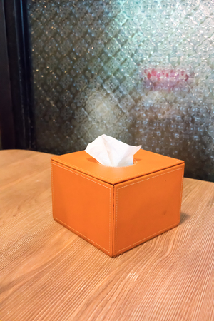 Orange leather cover tissue box isolated on wooden table against pattern glass.の写真素材