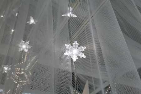 Illuminated LED icicle light against sheer fabric background for winter or Christmas decoration.