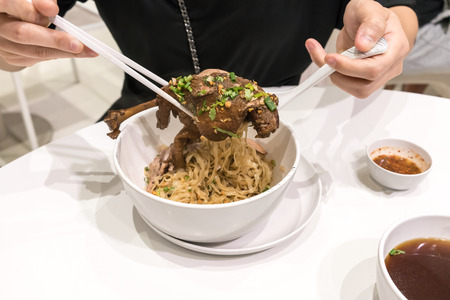Woman hand with chop stick and spoon holding stewed duck Noodle. Delicious Thai noodle with duck meat. Thai foodの写真素材