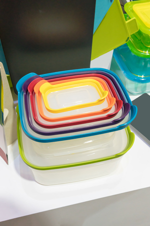 Stack of plastic containers with different sizes and lid colors on white table.