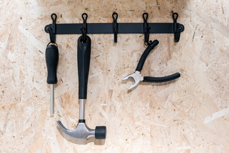 A set of hardware tools hanging on black metal hook against wooden wall.